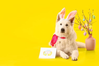 Tavşan kulaklı şirin köpek, dekor ve sarı arka planda Paskalya tebrik kartı.