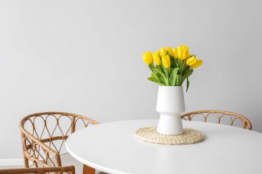 Yemek masasında, ışık duvarının yanında güzel laleleri olan vazo.