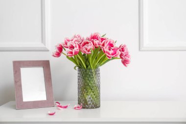 Laleli vazo ve beyaz duvarın yanındaki çekmecelerin üzerinde boş fotoğraf çerçevesi.