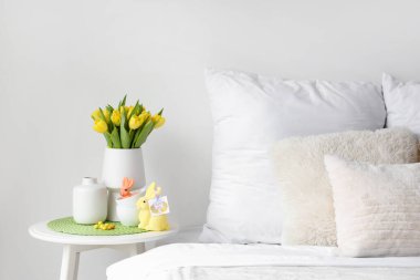 Laleli vazo, fincanlar ve rahat yatağın yanındaki masada Paskalya tavşanları.
