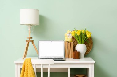 Modern dizüstü bilgisayarı, laleleri ve renk duvarına yakın tebrik kartı olan Paskalya tavşanı olan bir iş yeri.