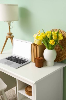 Modern laptop, vazo lale ve Paskalya tavşanı renkli duvarın yanında.