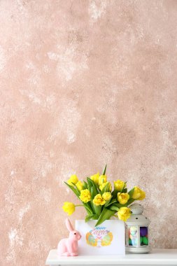 Güzel laleler, tebrik kartı, tavşan ve fener. Renk duvarının yanındaki masada Paskalya dekoru var.