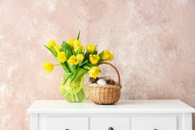 Paskalya yumurtaları ve renkli duvarların yanındaki masada laleler olan vazo.
