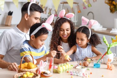 Küçük çocuklar ve aileleri mutfakta paskalya yumurtası boyuyorlar.