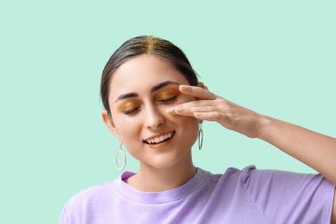 Yeşil arka planda olağandışı parlak makyajlı çekici bir genç kadın.