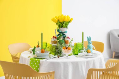 Şık bulaşık takımlarıyla yemek masası, Paskalya pastaları ve renkli duvarların yanında yumurtalar.