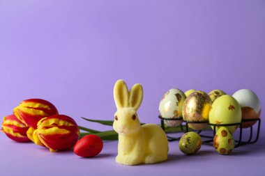 Mor arka planda boyanmış yumurtaları ve çiçekleri olan şirin Paskalya tavşanı.