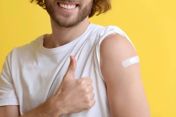 Young man with applied medical patch showing thumb-up on color background, closeup