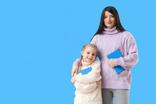 小女孩和她的妈妈穿着暖和的毛衣 带着蓝色背景的书 — 图库照片
