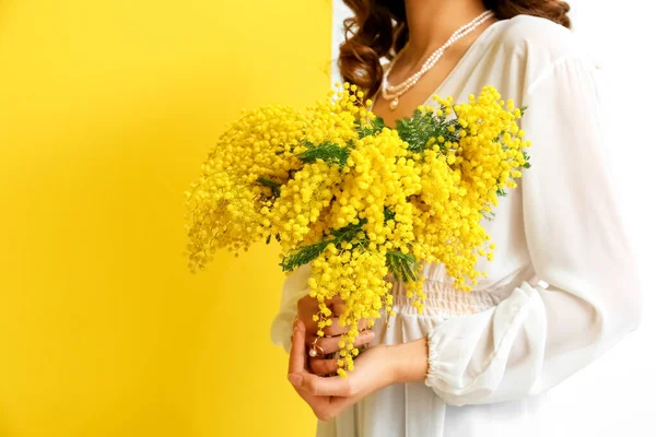 黄色と白の背景にミモザの花を持つ美しい若い女性 — ストック写真