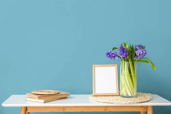 空白の写真フレームと色の壁の近くの花と花瓶付きの机に立つ — ストック写真