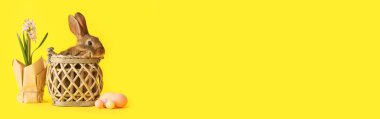Sepette sevimli pofuduk tavşan, sarı arka planda Paskalya yumurtası ve çiçekler, mesaj için yer var.