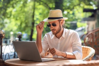 Caddedeki kafede dizüstü bilgisayarı olan yakışıklı bir genç.