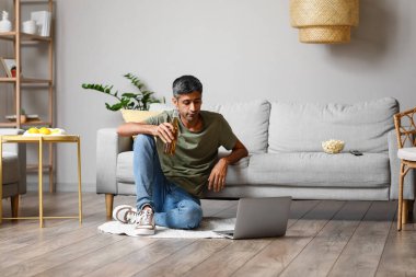 Evde dizüstü bilgisayarında bira şişesiyle film izleyen yakışıklı bir adam.