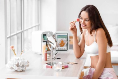 Evdeki makyaj masasına makyaj yapan güzel genç bir kadın.