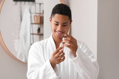 Genç Afro-Amerikalı adam banyoda cilt bakımı için serum kullanıyor.