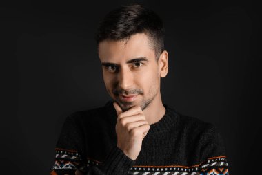 Esmer arka planda örülü süveter giyen yakışıklı bir genç.