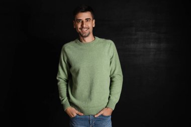 Esmer arka planda örülü süveter giyen yakışıklı bir genç.