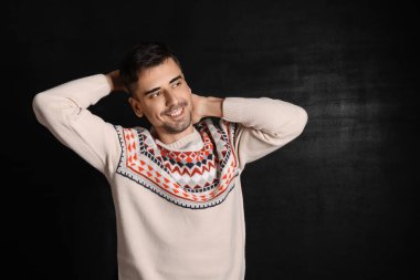 Esmer arka planda örülü süveter giyen yakışıklı bir genç.