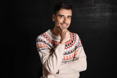 Esmer arka planda örülü süveter giyen yakışıklı bir genç.