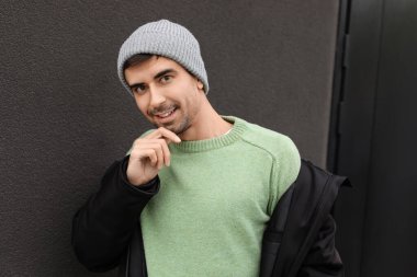 Esmer arka planda örülü süveter giyen yakışıklı bir genç.