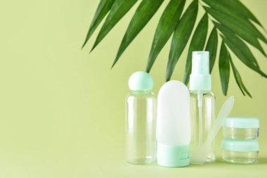 Yeşil arka planda seyahat şişeleri, kavanozlar ve palmiye yaprakları.