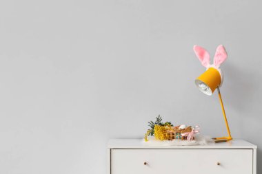 Paskalya yumurtaları, mimoza çiçekleri ve ışık duvarının yanındaki rafta duran lamba sepeti.