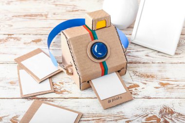 El yapımı karton fotoğraf makinesi ve ahşap masada resimler.