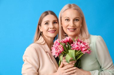 Annesi ve mavi arka planda bir buket lale olan genç bir kadın.