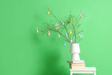 Kitap yığını, ağaç dalları olan vazo ve renkli duvarın yanındaki merdivenlerde Paskalya yumurtası.