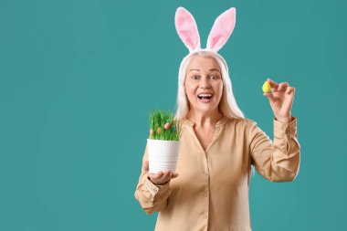 Tavşan kulaklı olgun bir kadın, yeşil arka planda Paskalya yumurtası ve bitkisi.