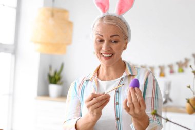 Evde paskalya yumurtası boyayan olgun bir kadın.
