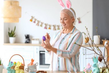 Evde paskalya yumurtası boyayan olgun bir kadın.