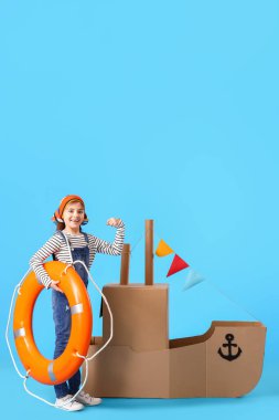 Mavi arka planda karton gemiyle oynayan komik küçük kız.