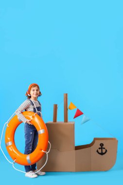 Mavi arka planda karton gemiyle oynayan komik küçük kız.