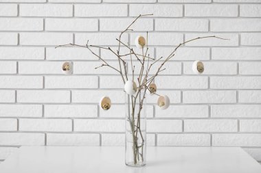 Kırık paskalya yumurtalarıyla süslenmiş ağaç dalları beyaz tuğla duvarın yanındaki masada vazoda.