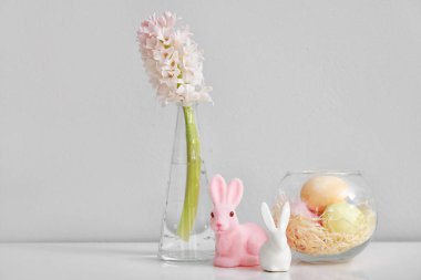 Sümbül çiçekli vazo, Paskalya yumurtası ve ışık duvarının yanındaki masada tavşanlar.