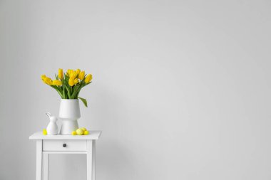 Sarı laleli vazo, Paskalya yumurtası ve ışık duvarının yanındaki masada tavşan.
