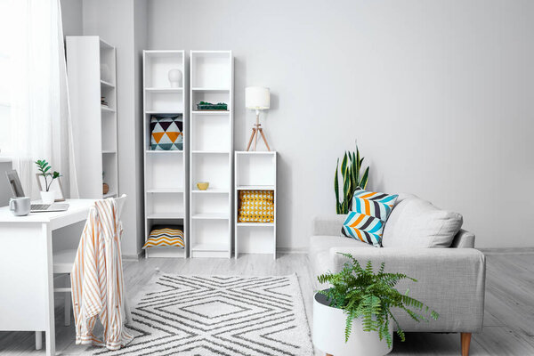 Interior of light living room with modern workplace, sofa and big shelving unit