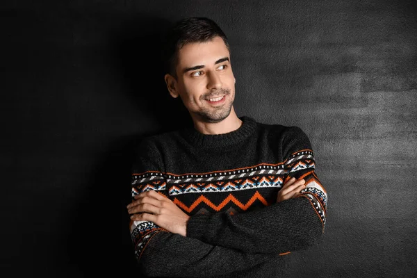 Esmer arka planda örülü süveter giyen yakışıklı bir genç.