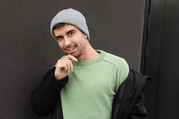 Esmer arka planda örülü süveter giyen yakışıklı bir genç.