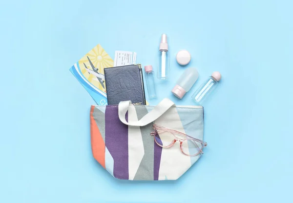 Bag with documents, eyeglasses and empty travel bottles on color background