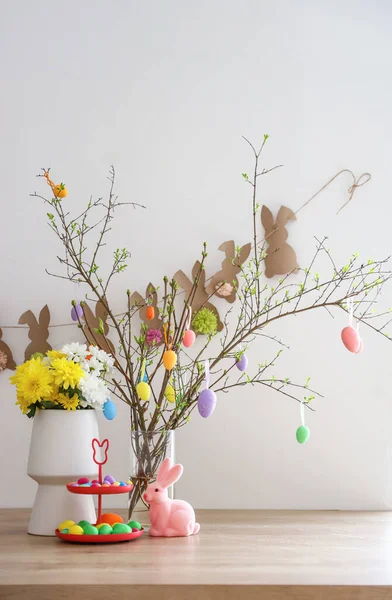 Paskalya yumurtalarının, güzel çiçeklerin ve şık dekorun yanında beyaz duvarın yanında dur.