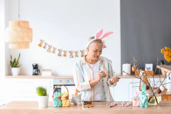 Evde paskalya yumurtası boyayan olgun bir kadın.