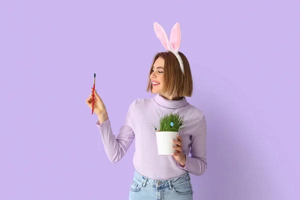 美丽的年轻女子 有兔子耳朵 刷子和家庭植物的色彩背景 复活节庆祝活动 — 图库照片