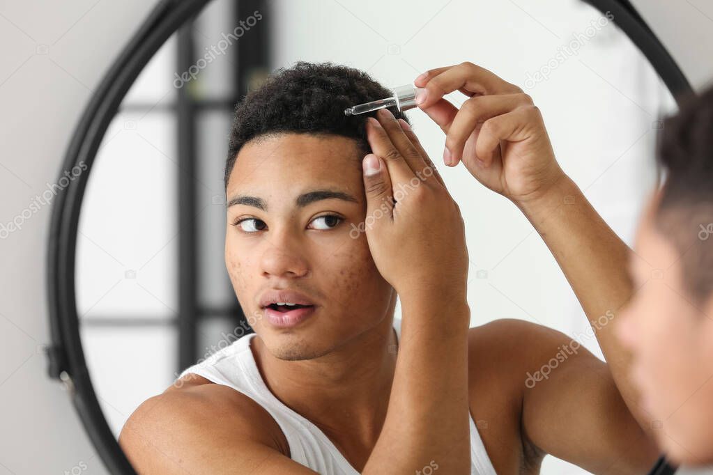 Young African-American guy using serum for hair growth in bathroom