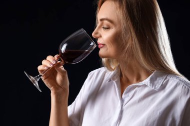 Kadın şarap garsonu koyu arkaplanda şarap tadıyor