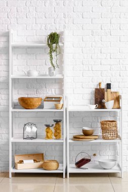Beyaz tuğla duvarın yanında mutfak aletleri olan modern raf üniteleri.