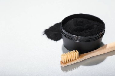 Aktif hale getirilmiş kömür diş tozu ve beyaz arka planda diş fırçası olan kavanoz.